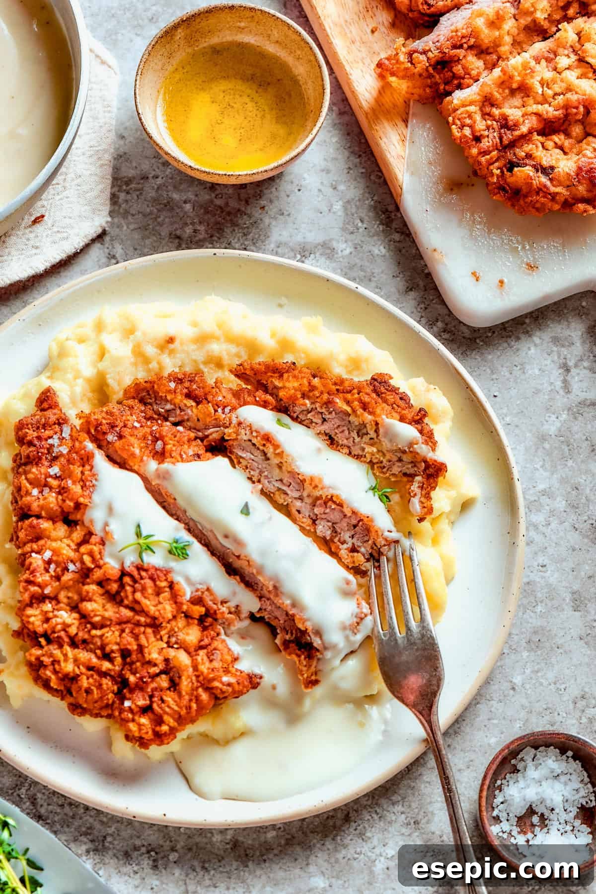 Golden Fried Country Steak 15 Sliced chicken fried steak served over mashed potatoes, and a fork is resting on top of the meat.