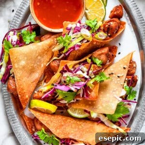 Chicken wonton tacos arranged on an oval platter with a bowl of sauce set right next to the tacos.