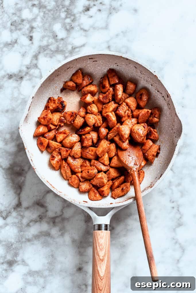 A spoon stirs the chicken as it browns and cooks evenly in the skillet, achieving perfect caramelization.