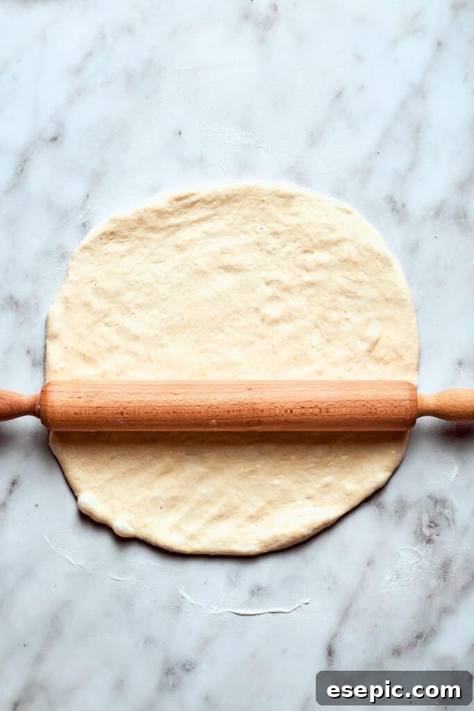 A rolling pin skillfully rolls out the deep dish pizza dough on a floured surface, preparing it for the pan.