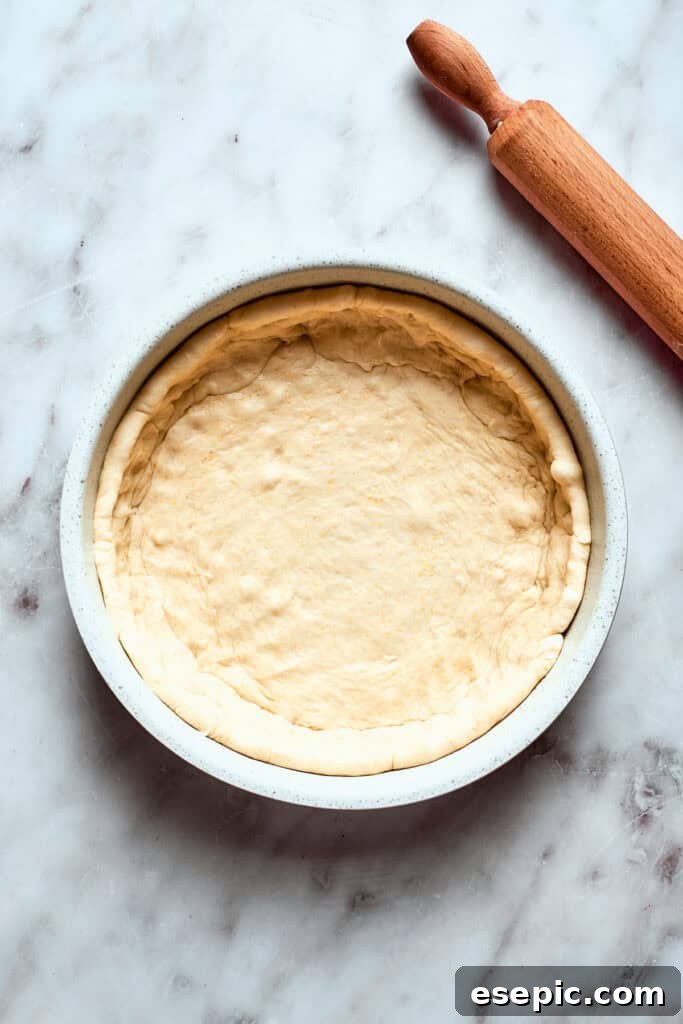 The deep dish pizza dough is carefully fitted into a deep-sided baking pan, ready for its layers of deliciousness.