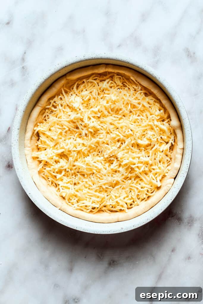 Generous layers of shredded cheese are added directly onto the deep dish pizza dough.