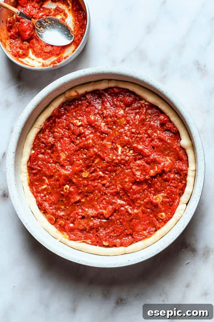 The thick, rich tomato sauce is generously added over the cheese layer of the deep dish pizza.