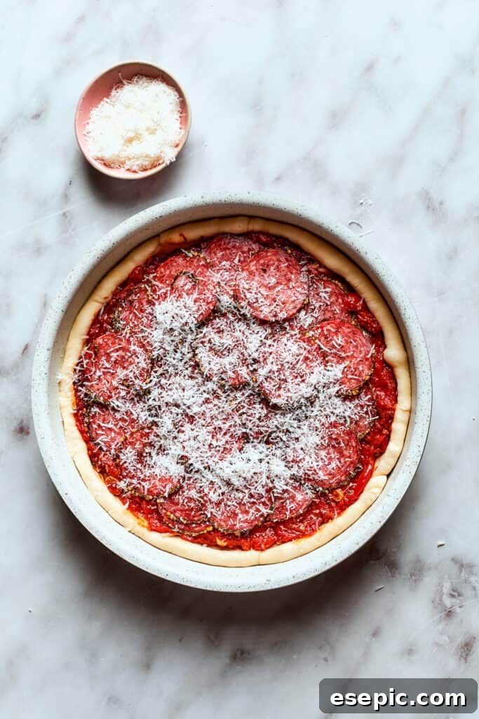 Parmesan cheese is generously scattered over the top of the deep dish pizza, ready for baking.