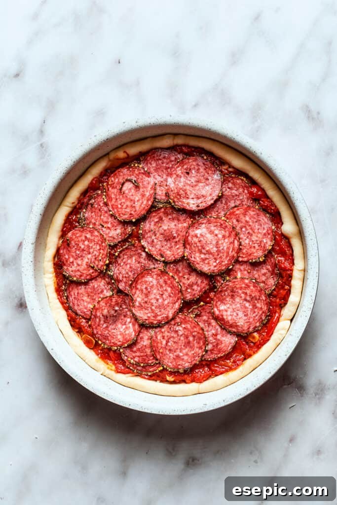 Classic pepperoni slices are meticulously arranged on top of the deep dish pizza, creating an appetizing pattern.