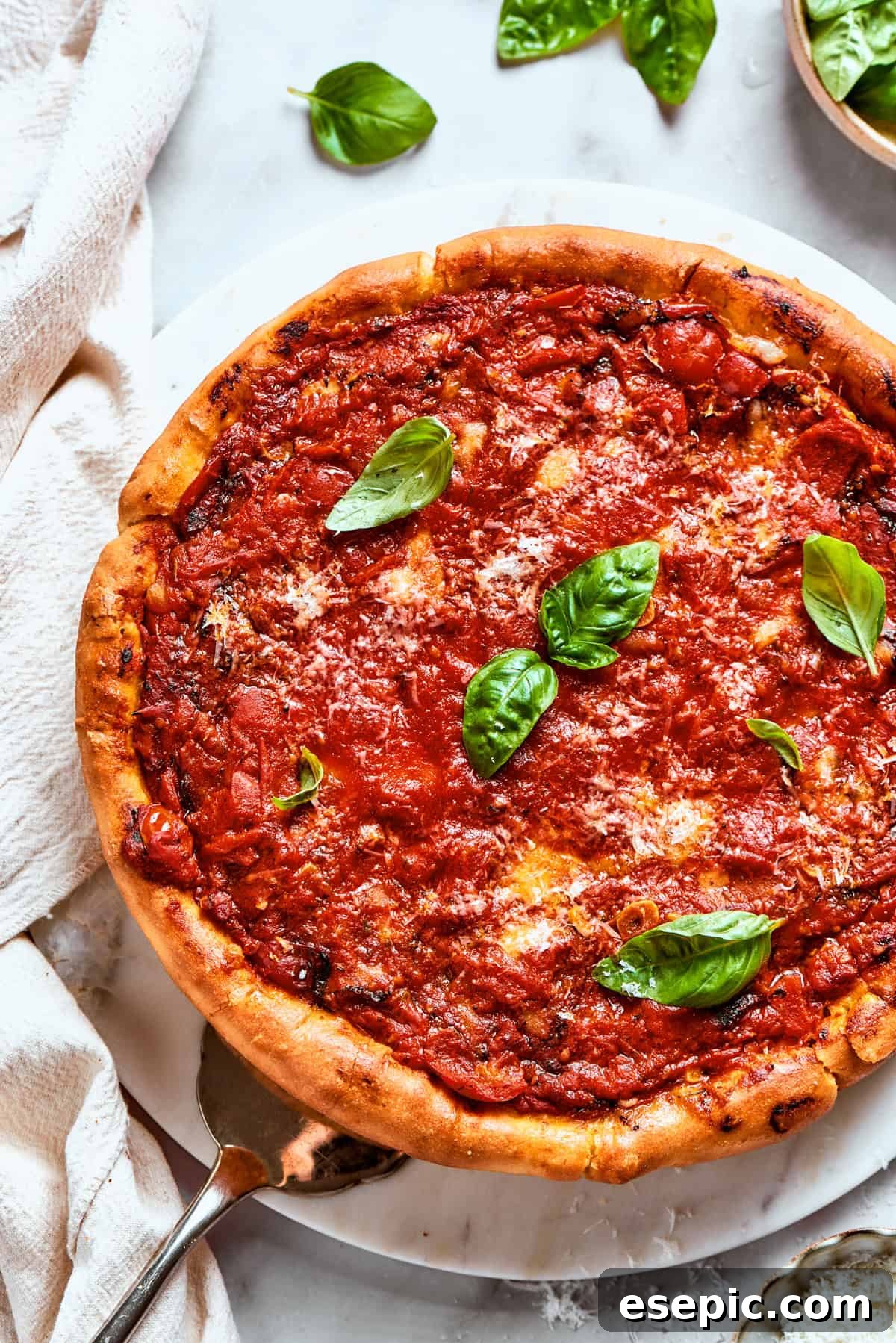 Overhead image of a beautifully golden deep dish pizza, richly topped with tomato sauce and fresh basil leaves, hot out of the oven.