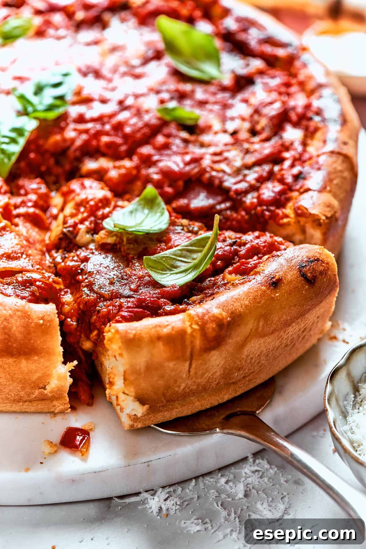 Serving spoon lifting out a perfectly baked slice of deep dish pizza, revealing its thick layers of melted cheese, robust sauce, and savory pepperoni.