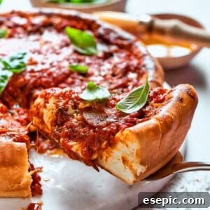 Serving spoon lifting out a slice of deep dish pizza, showcasing its thick layers of cheese, sauce, and toppings.