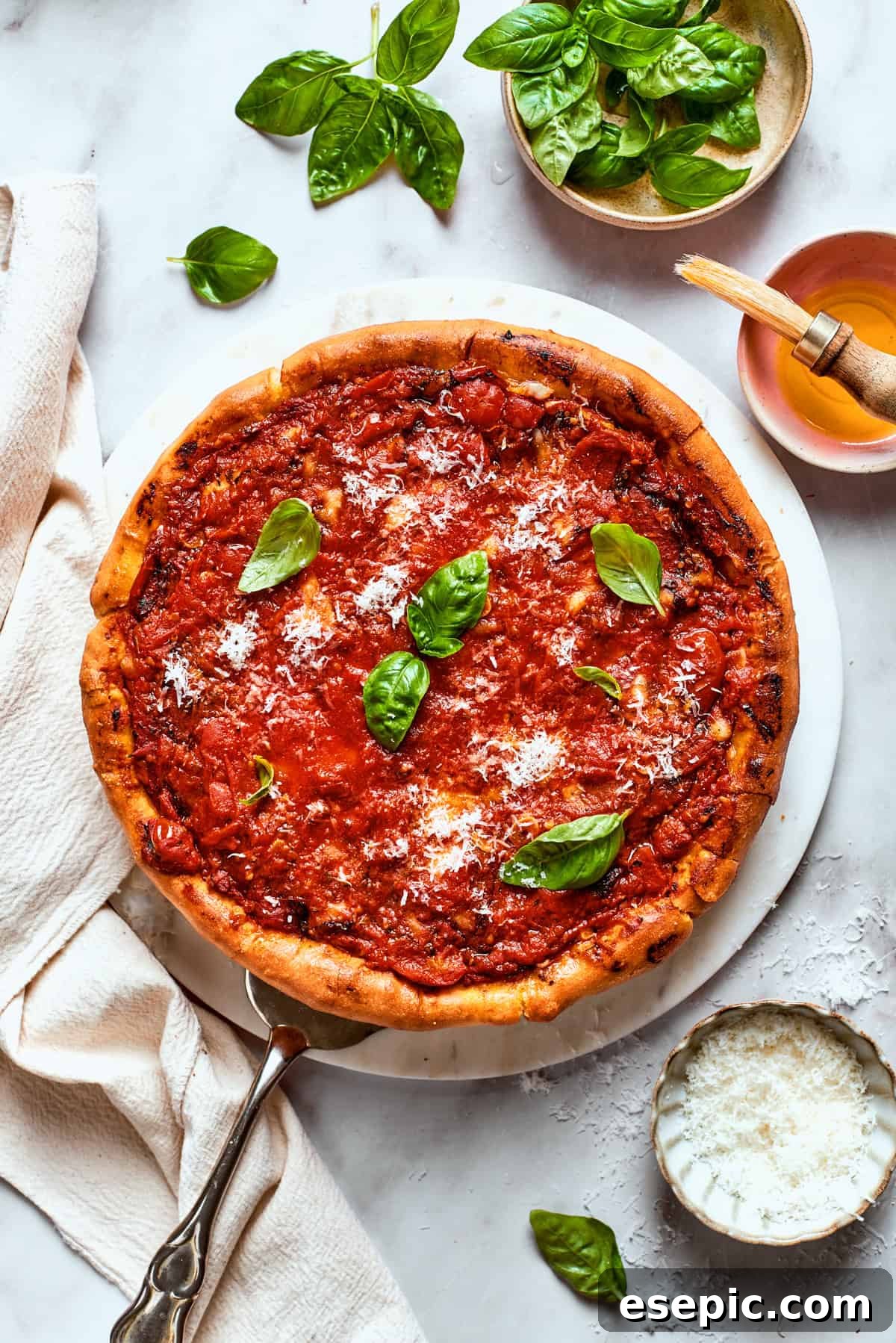 Overhead image of a freshly baked deep dish pizza, topped with a rich tomato sauce and garnished with bright green fresh basil leaves, ready to be sliced.