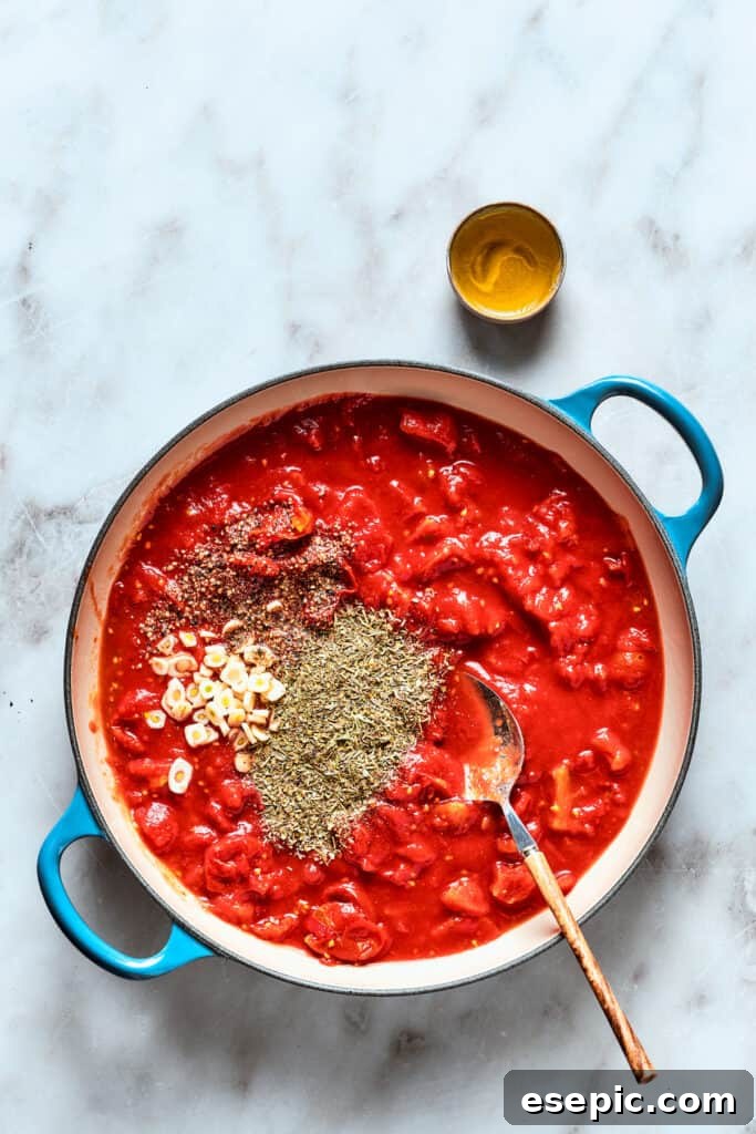 The thick and rich sauce for deep dish pizza, simmering in a saucepan with a scattering of Italian spices on top.