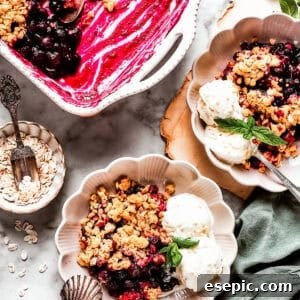 Overhead image of two dessert bowls of blueberry crisp served with scoops of ice cream. There is a baking dish with the crisp placed near the bowls.