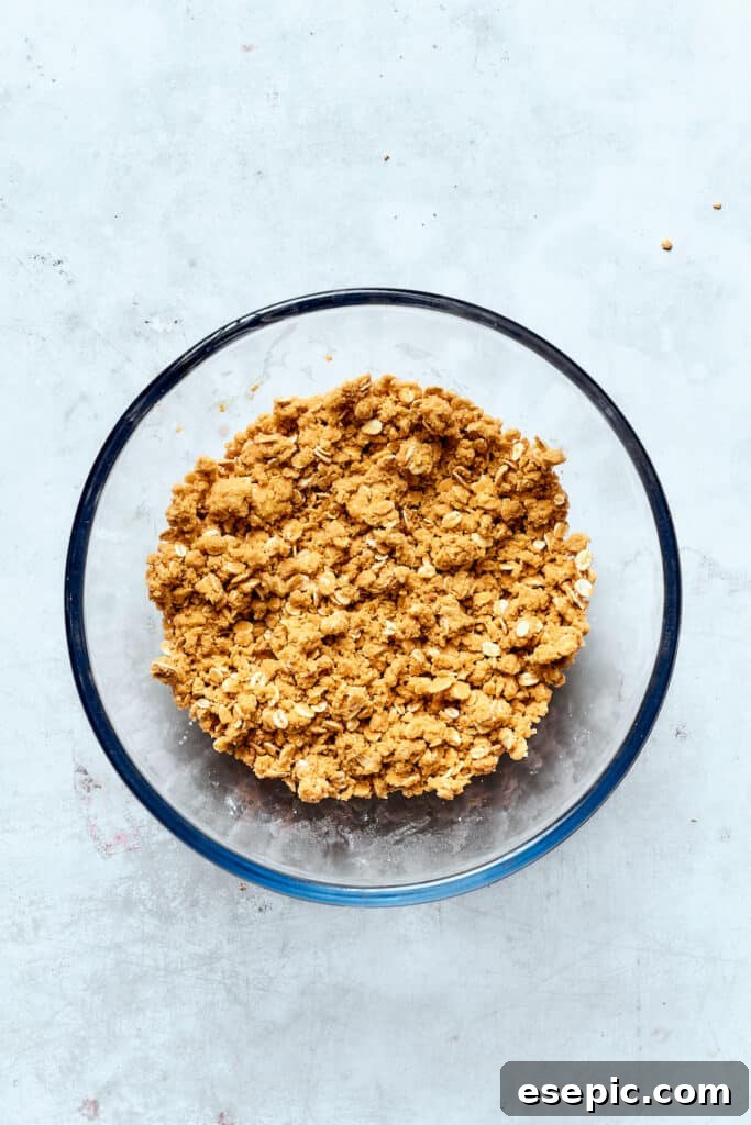 The crucial step of cutting cold butter into the topping mixture until it forms coarse, crumbly pieces. Cold, cubed butter is being cut into the dry crisp topping mixture using hands, creating a crumbly texture.