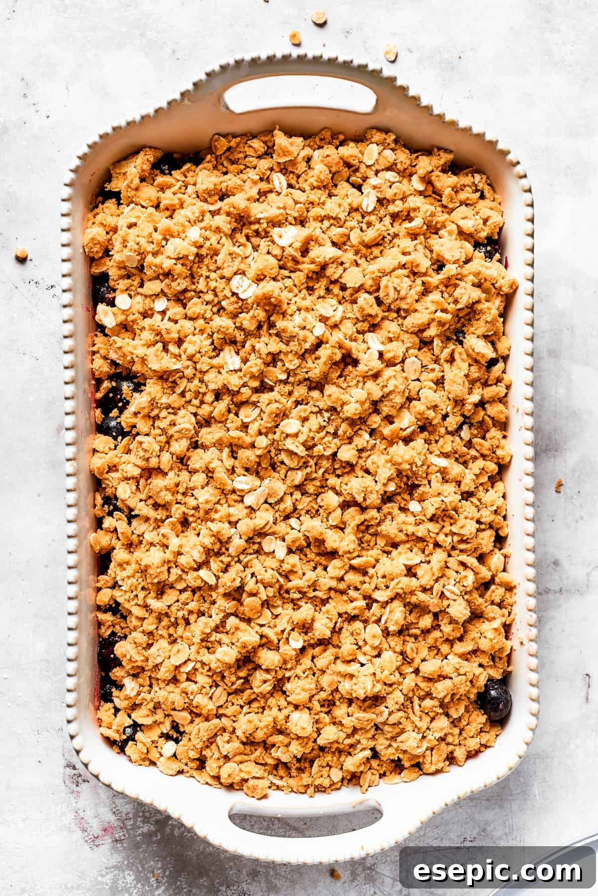 The final assembly: topping the vibrant blueberry mixture with the rich, buttery oats topping before baking. The buttery oat crumble mixture is generously sprinkled over the blueberry filling in a baking dish, ready for baking.