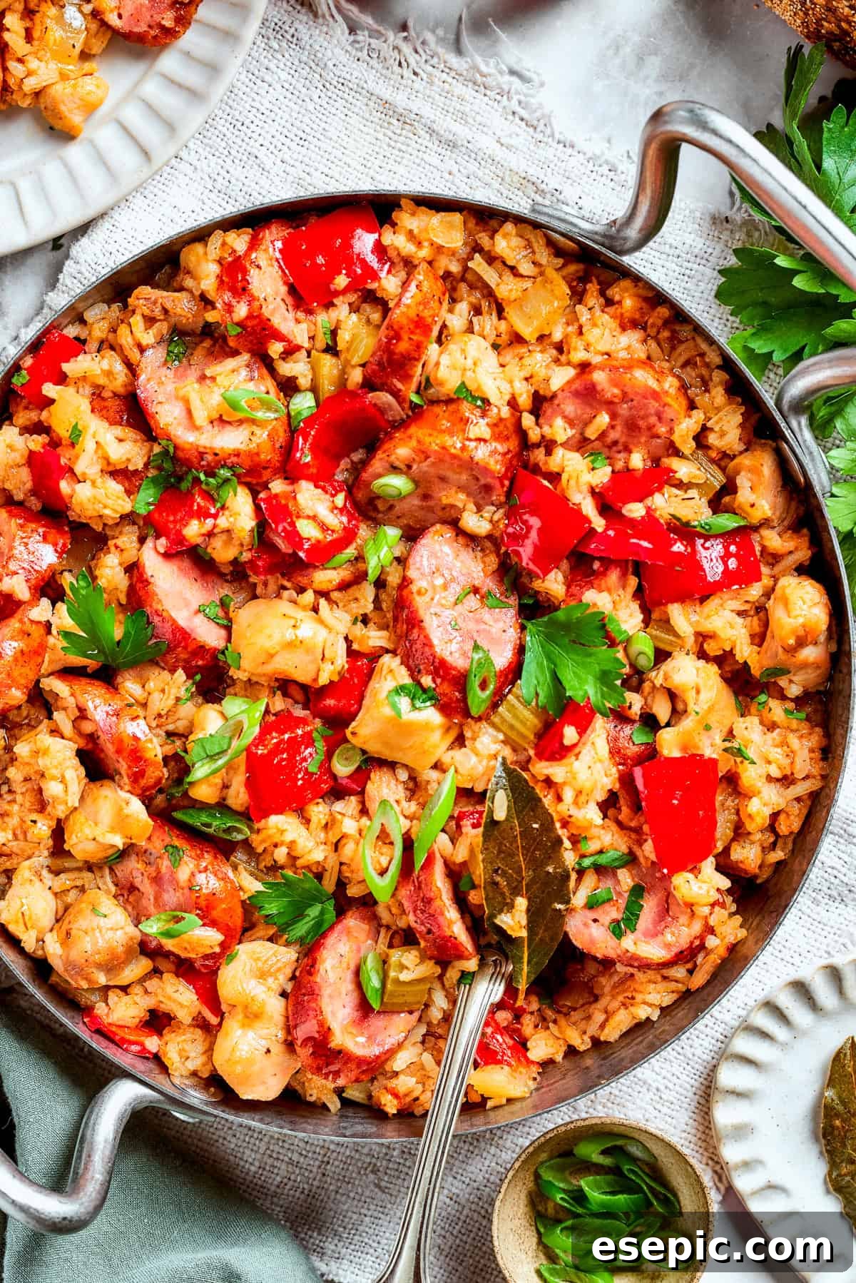Image of a pan with jambalaya featuring a bed of rice topped with chicken bites, sliced sausages, and diced red bell peppers.