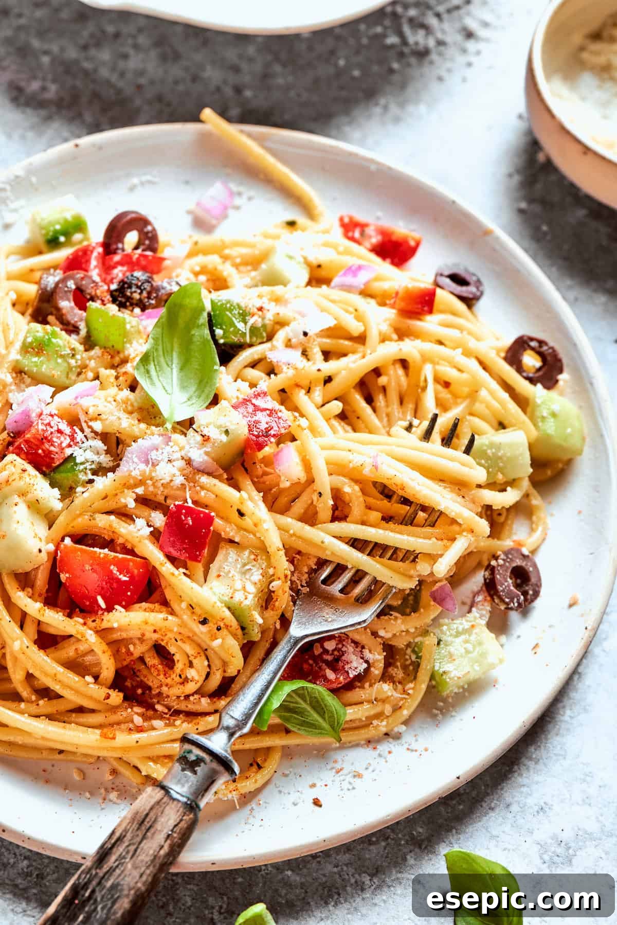 A fork lifts a generous portion of spaghetti salad from a plate, showing the long noodles and colorful vegetable pieces.