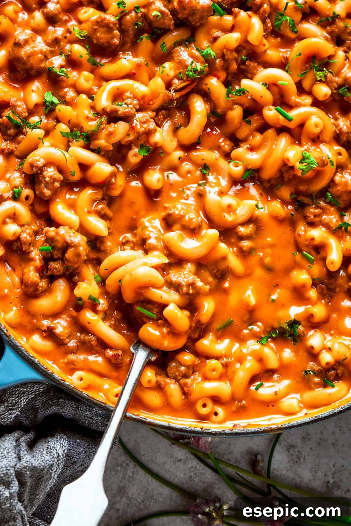 A spoon stirring through homemade hamburger helper in a skillet, showcasing the rich, creamy texture and generous amount of ground beef and pasta.