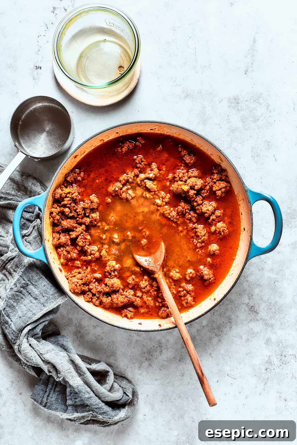 Ground beef cooking in beef broth and tomato puree in a large skillet, forming the base of the sauce.