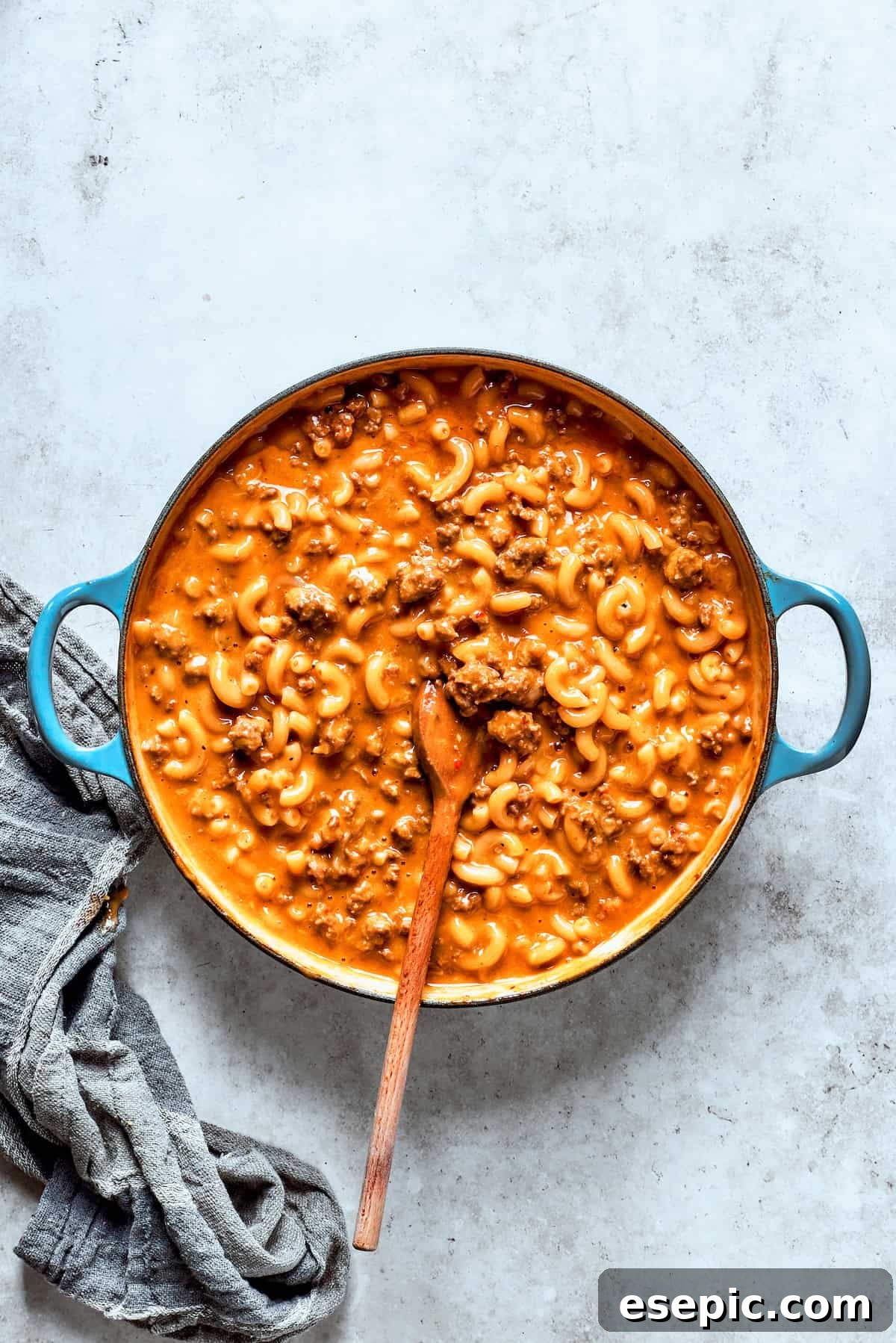 Shredded cheddar cheese and heavy cream being stirred into the pot of finished hamburger helper, creating a creamy and cheesy texture.