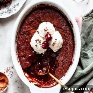 Chocolate cake in a casserole dish garnished with vanilla ice cream scoops, two cherries, with a gold-colored spoon set inside the cake.
