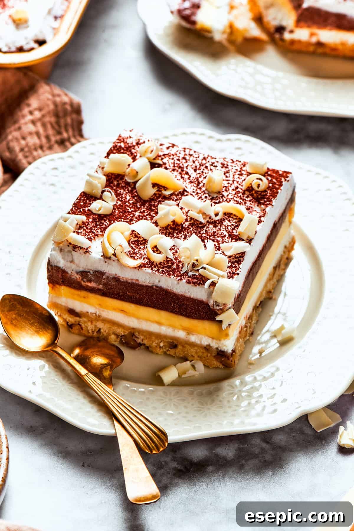 Pecans and white chocolate shavings top a slice of sex in a pan.