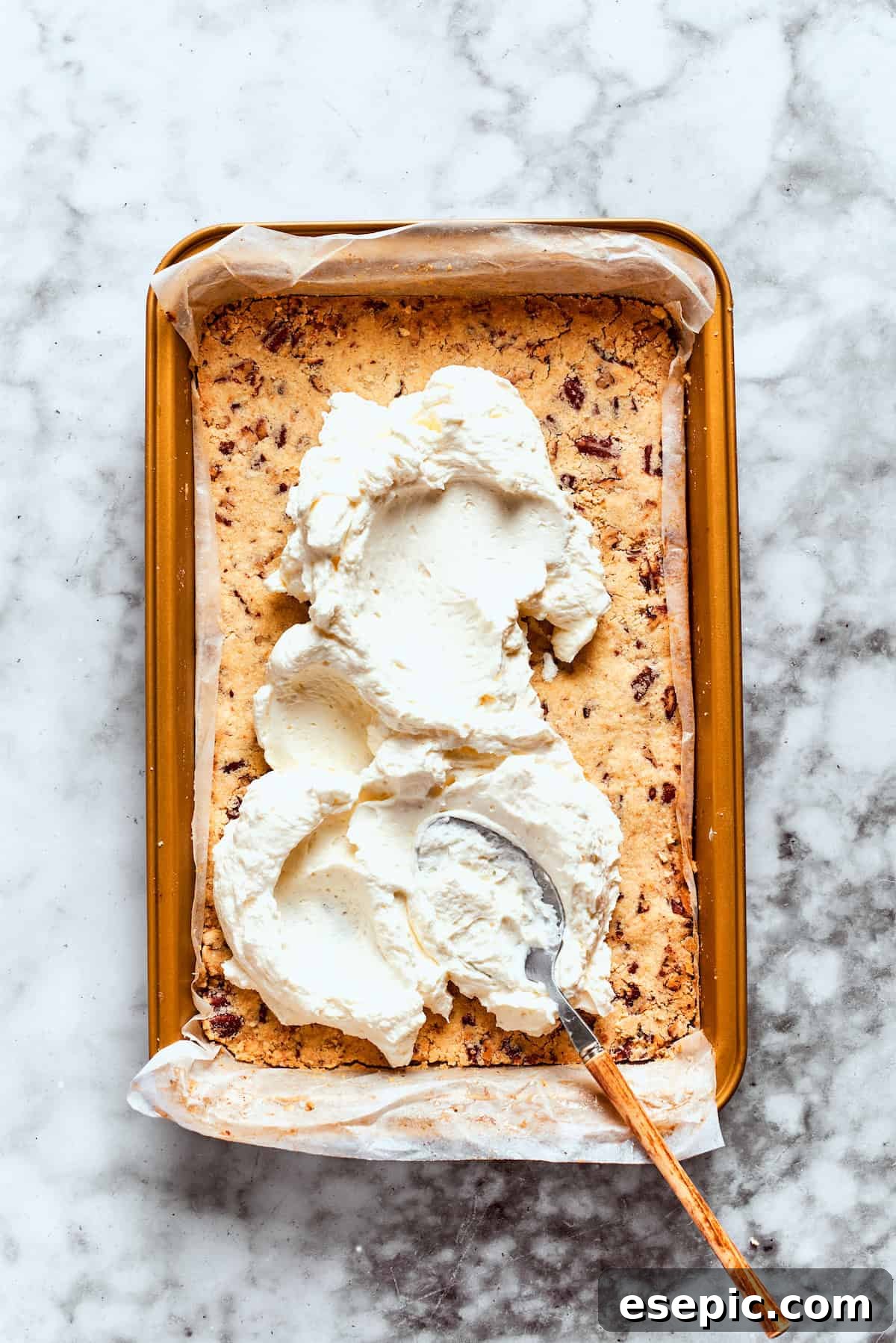 The fluffy cream cheese layer is spread evenly over the cooled pecan crust.