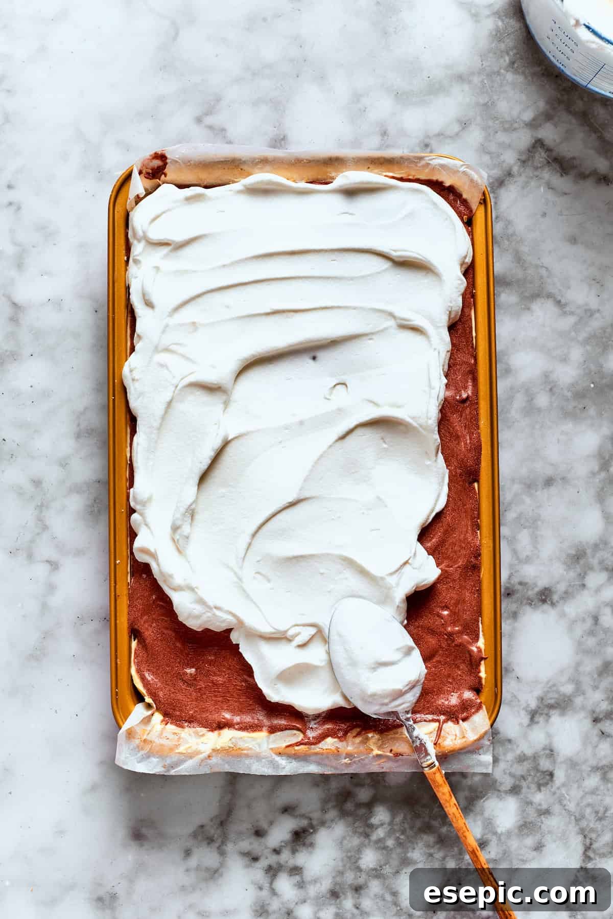 A generous layer of Cool Whip is spread smoothly over the chocolate pudding, ready for chilling.