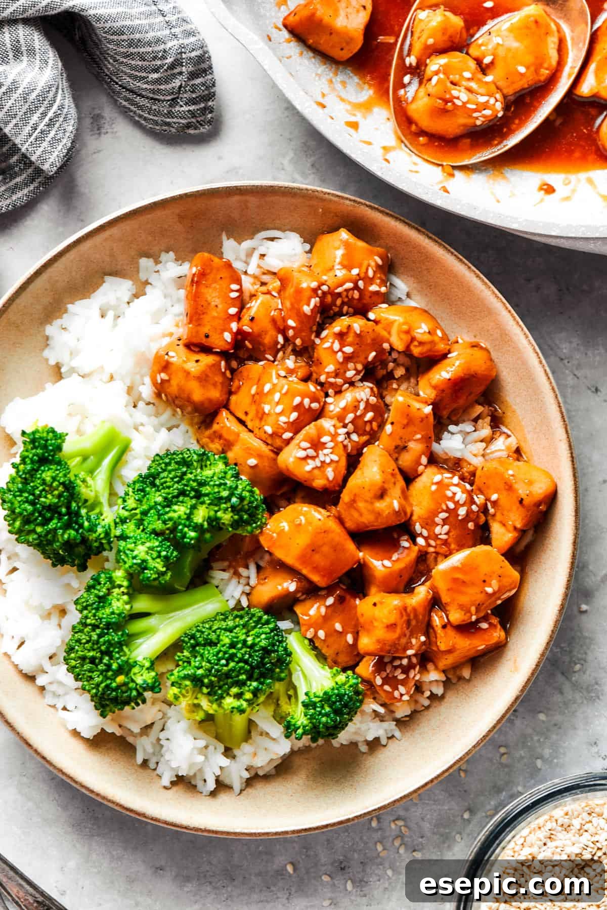 This Teriyaki Chicken Recipe folds tender bites of chicken into a thick, homemade teriyaki sauce for a savory and flavorful dish. Teriyaki chicken pieces served over rice in a bowl with a side of broccoli.