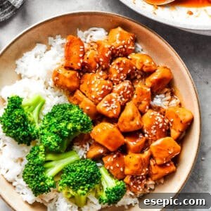 Teriyaki chicken pieces served over rice in a bowl with a side of broccoli.