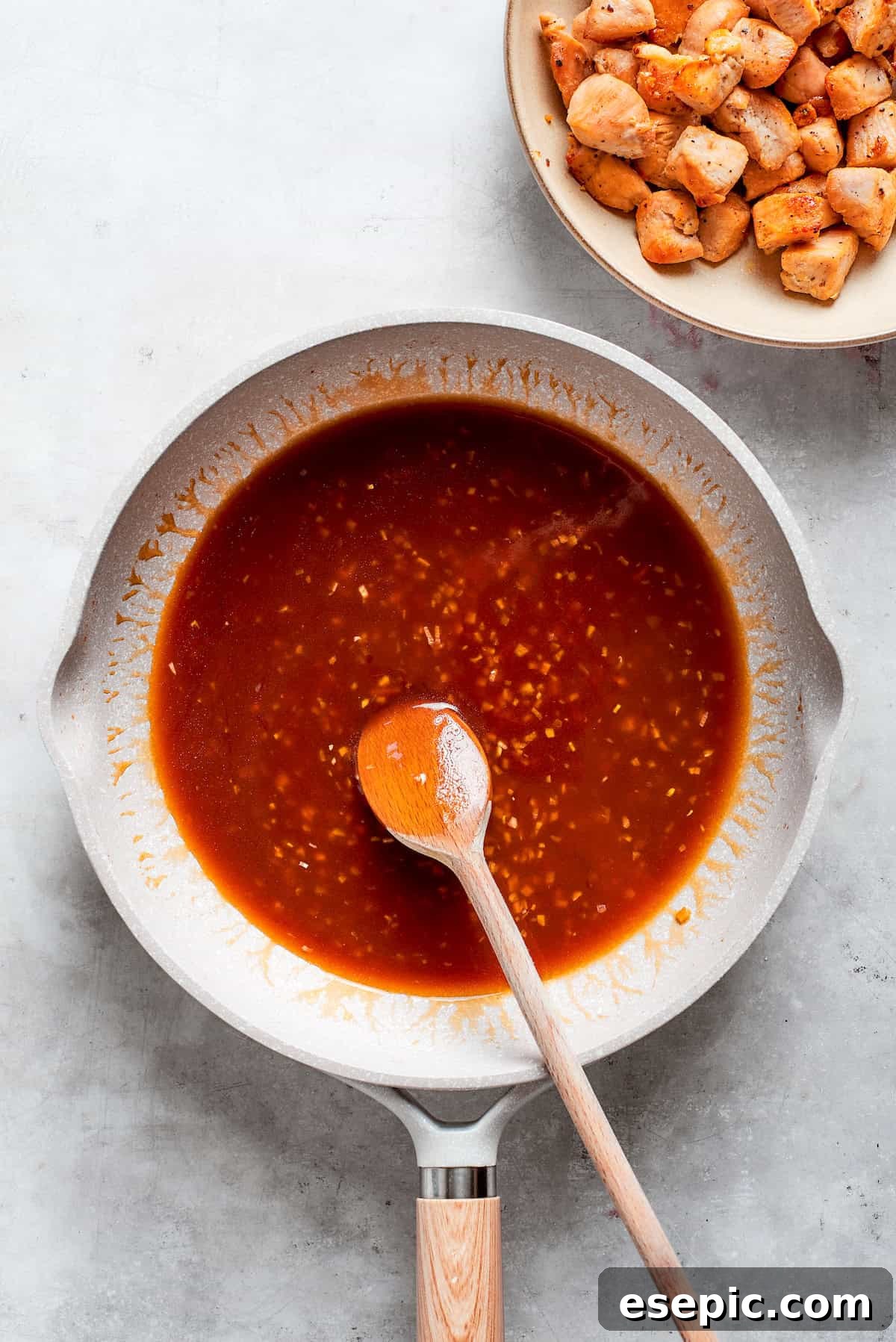This Teriyaki Chicken Recipe folds tender bites of chicken into a thick, homemade teriyaki sauce for a savory and flavorful dish. A spoon combines the teriyaki sauce in a pan.