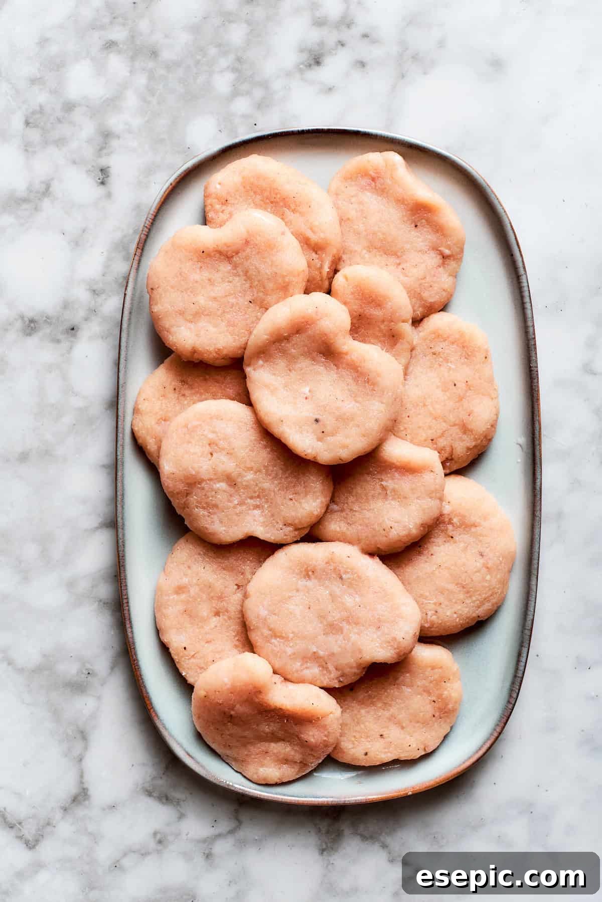 This easy homemade Chicken Nuggets Recipe features perfectly cooked homemade chicken nuggets that are crispy outside and juicy on the inside. The nuggets are formed and placed on a plate.