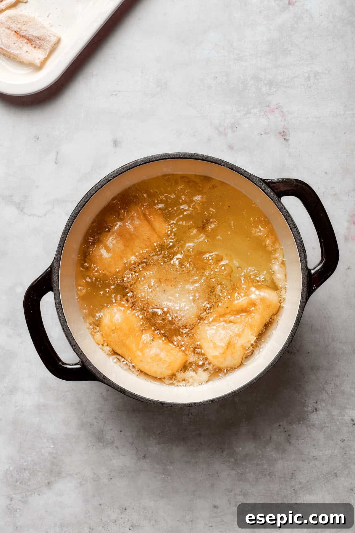 Pieces of beer-battered fish sizzling and turning golden brown in a deep pot of hot oil, indicating they are actively frying.