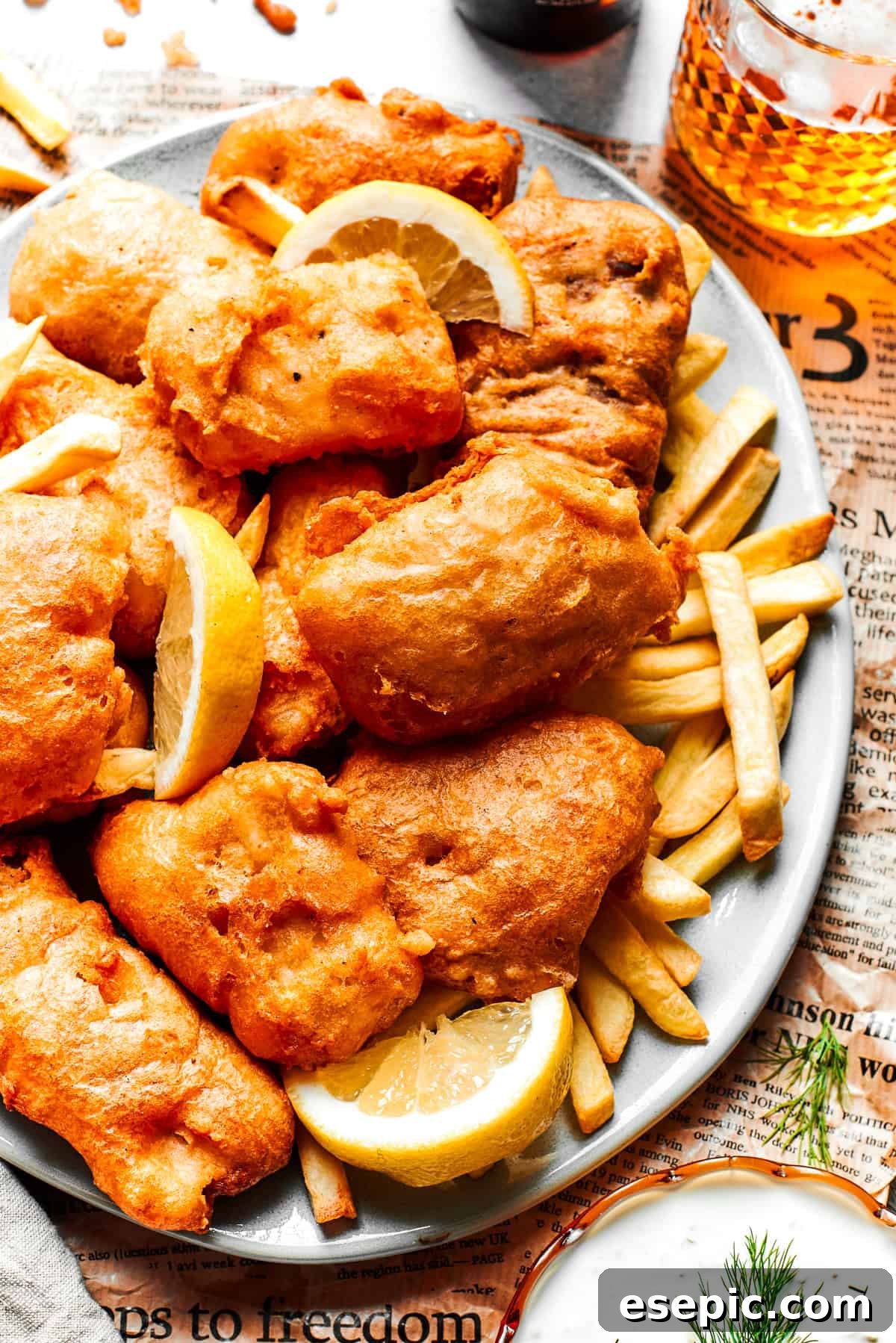 A large platter presenting an abundance of perfectly fried beer battered fish fillets, served with a generous side of golden French fries, evoking a hearty pub-style meal.