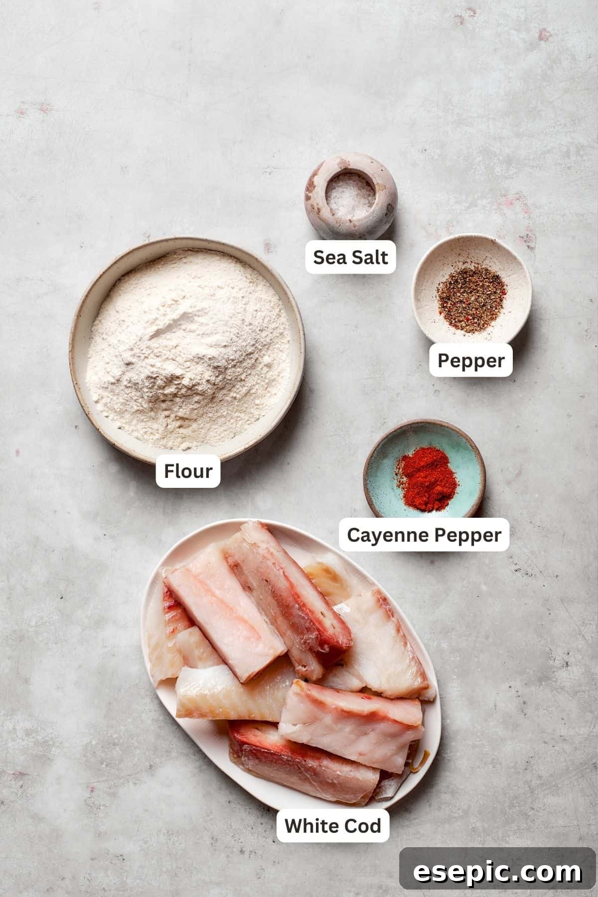 Close-up of fresh, raw ingredients laid out on a clean surface, including fish fillets, flour, a bottle of beer, and various spices, ready for making beer battered fish.
