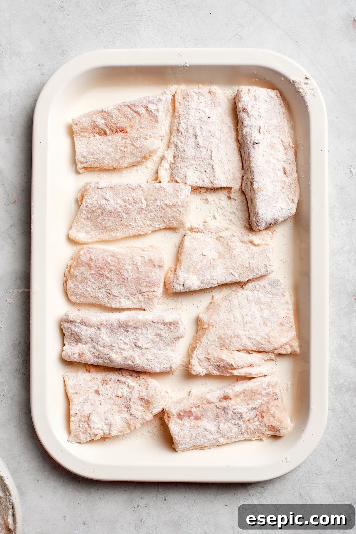 Several floured fish pieces neatly arranged on a baking tray, ready for the next step of battering and frying.