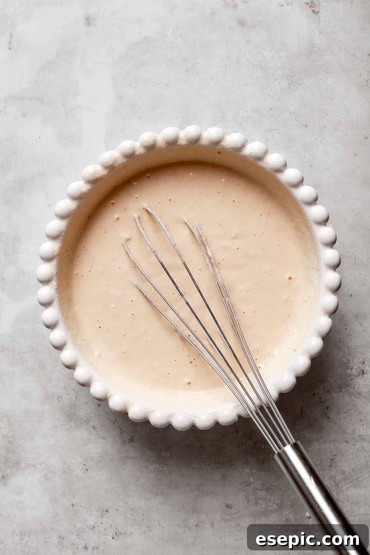A whisk vigorously mixing cold beer into the dry batter ingredients in a bowl, creating a smooth, effervescent batter.