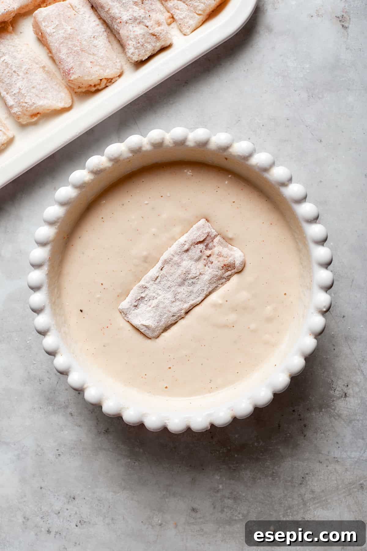 A floured piece of fish being gently submerged into the beer batter, ensuring a full and even coating before frying.
