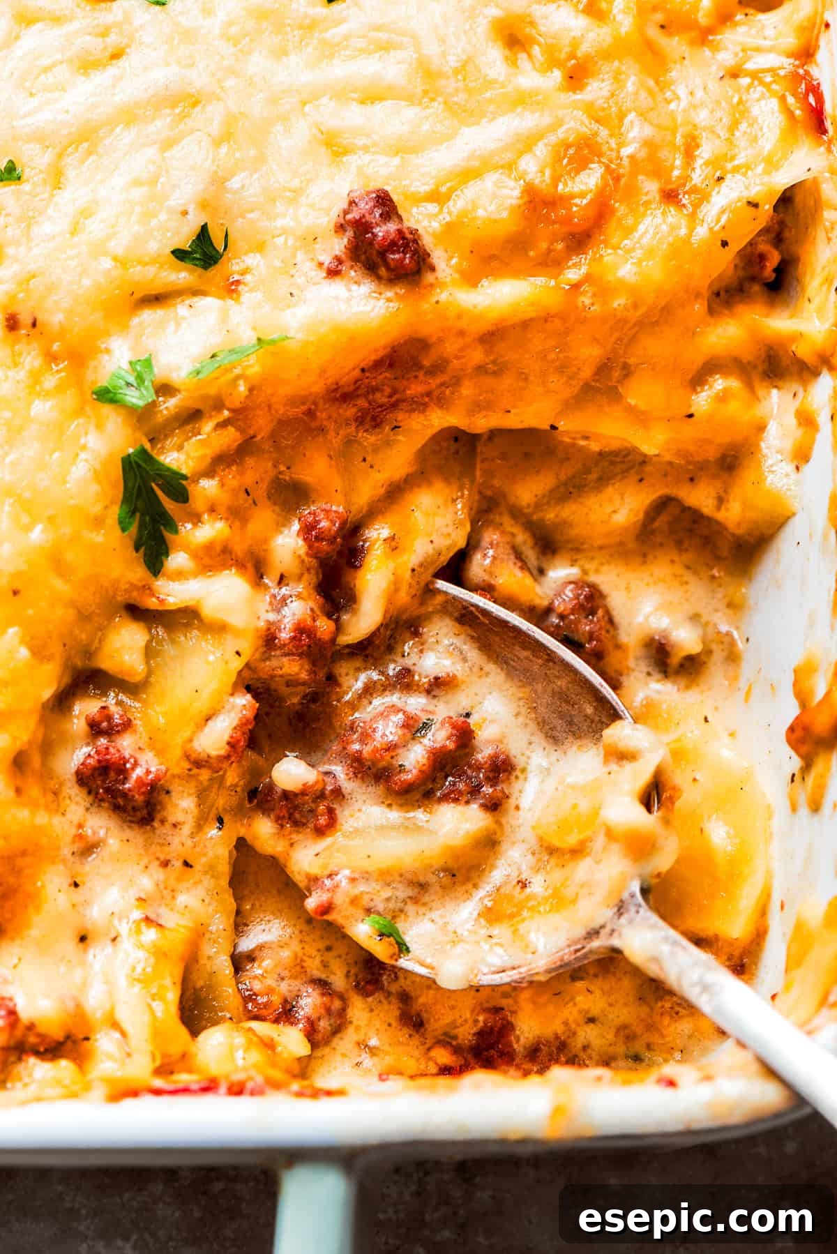 A spoon mixing through a casserole with ground beef and potatoes.