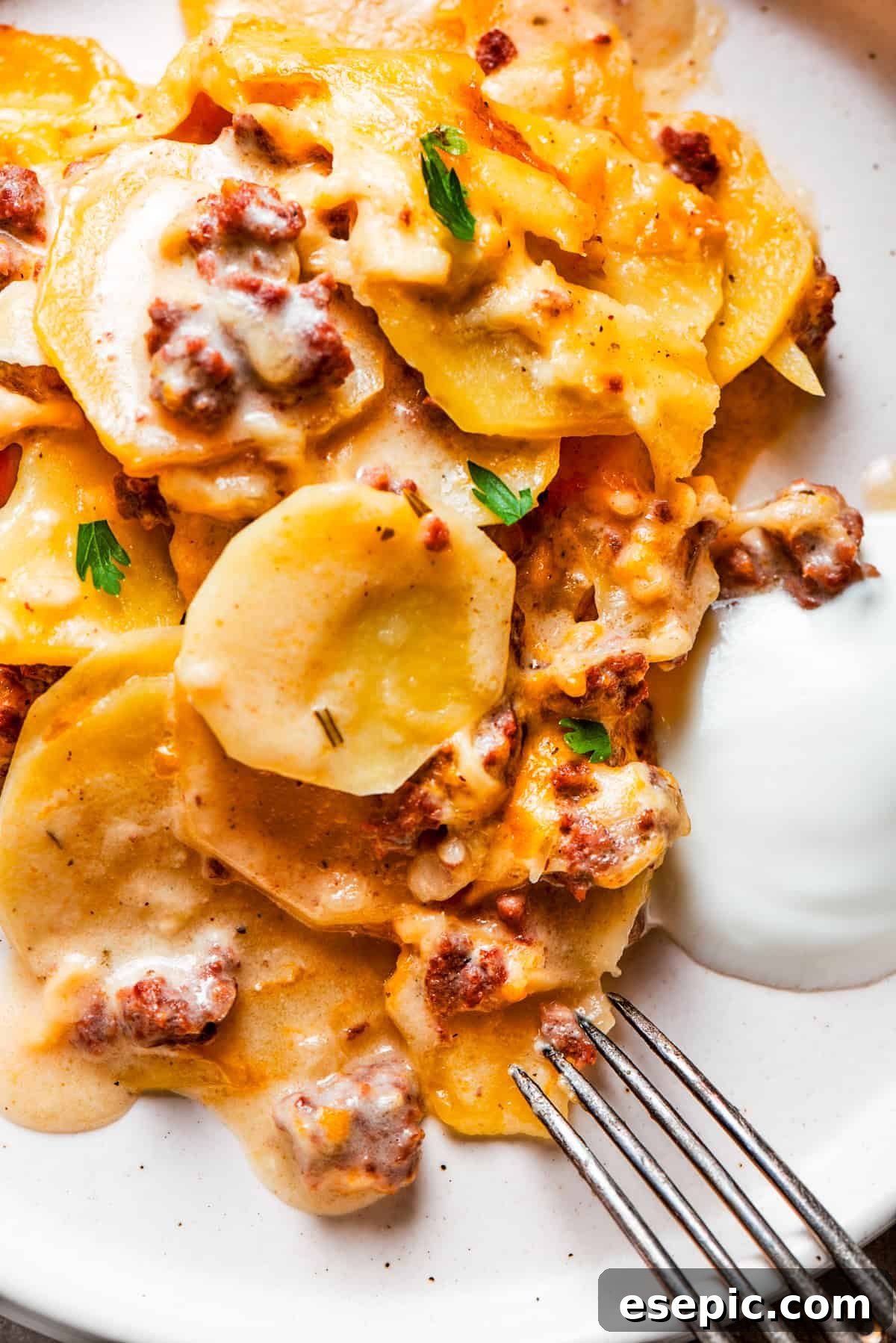 Close-up image of cooked sliced potatoes and ground beef served on a dinner plate with a fork set next to the food.