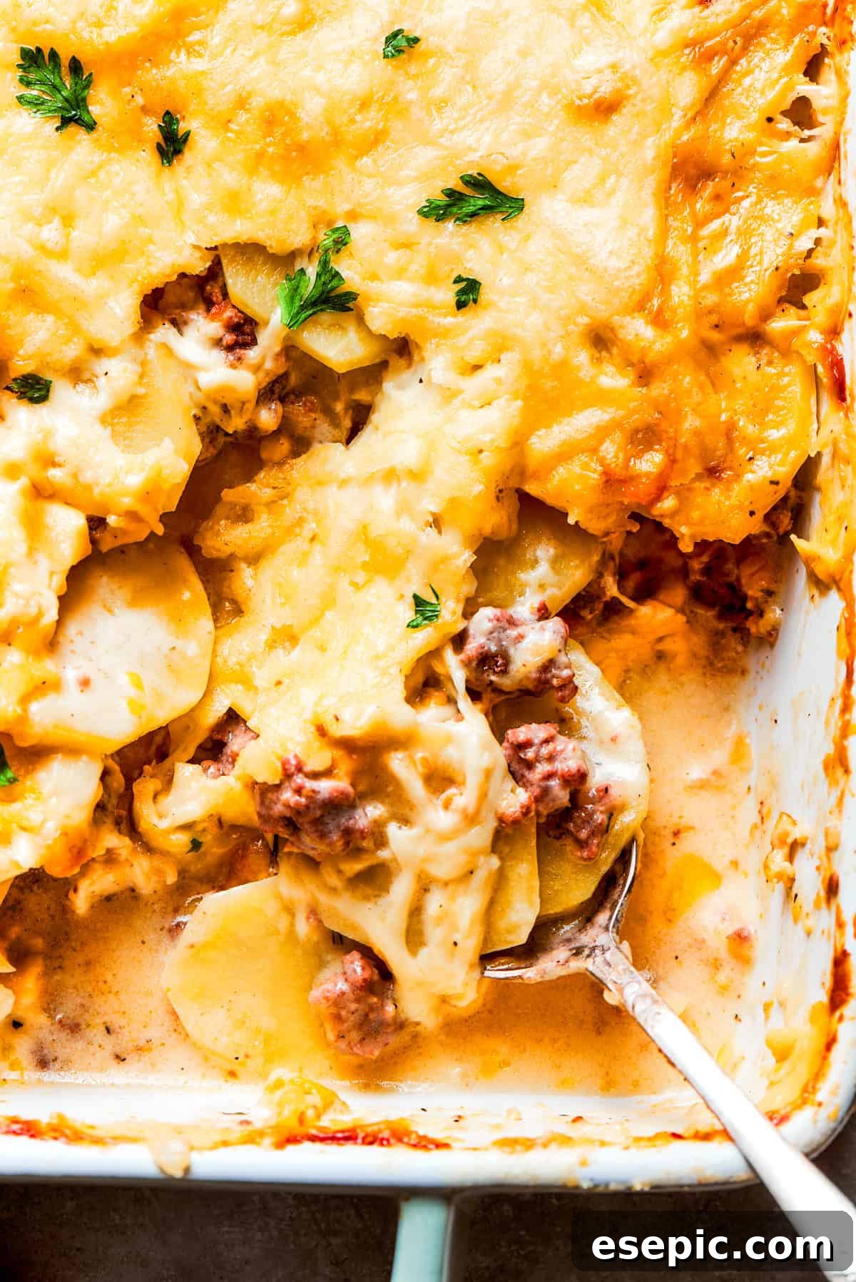 Up close photo of a spoon mixing through a casserole with ground beef and potatoes.