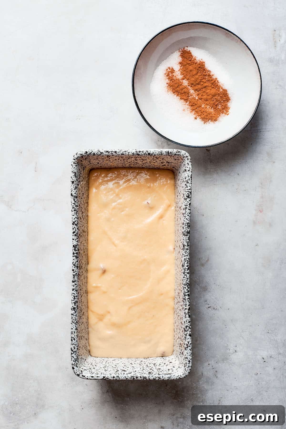 Amish friendship bread batter in a loaf pan with cinnamon sugar next to it.