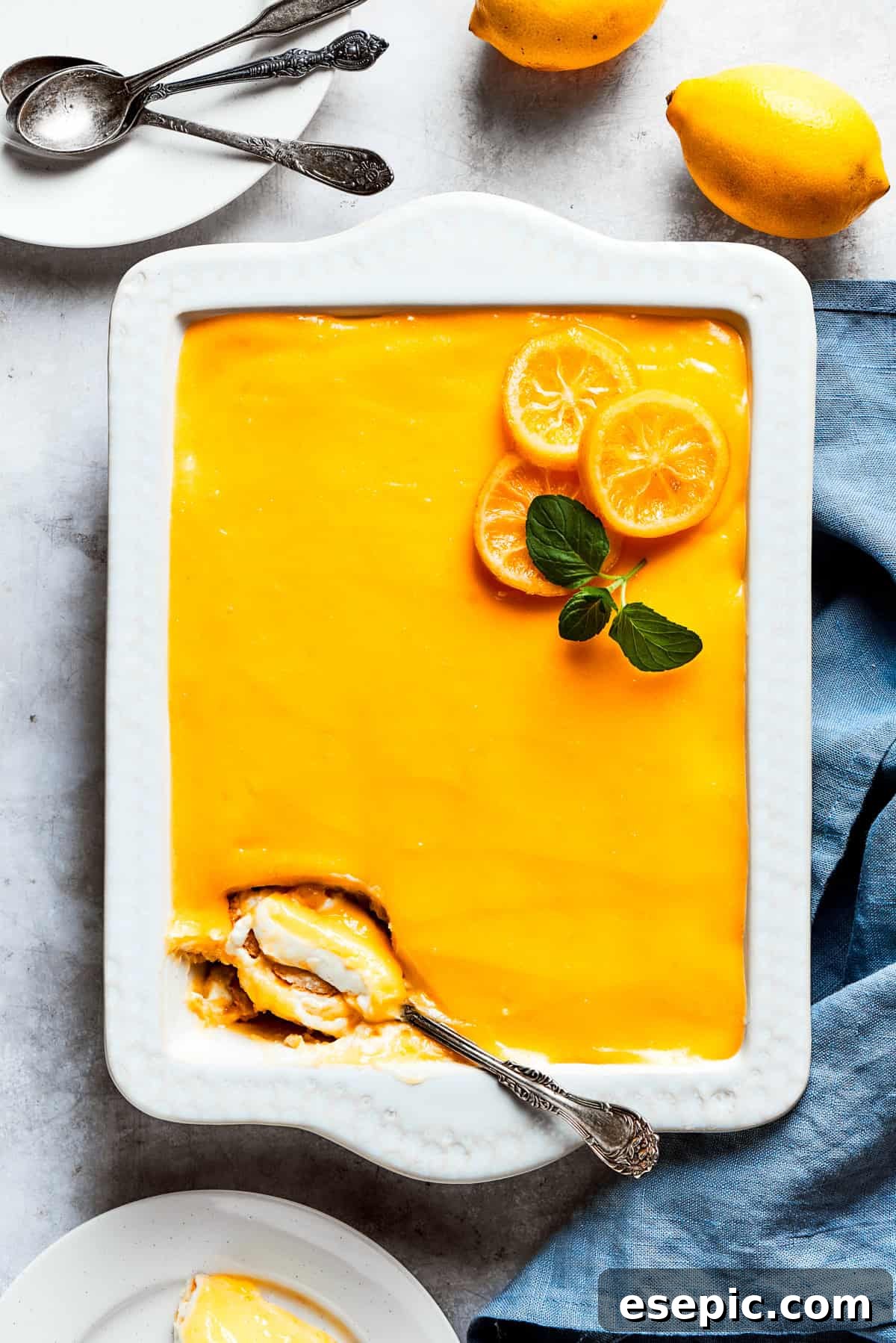 A serving spoon is digging into the corner of a pan of lemon tiramisu, showcasing its creamy layers.