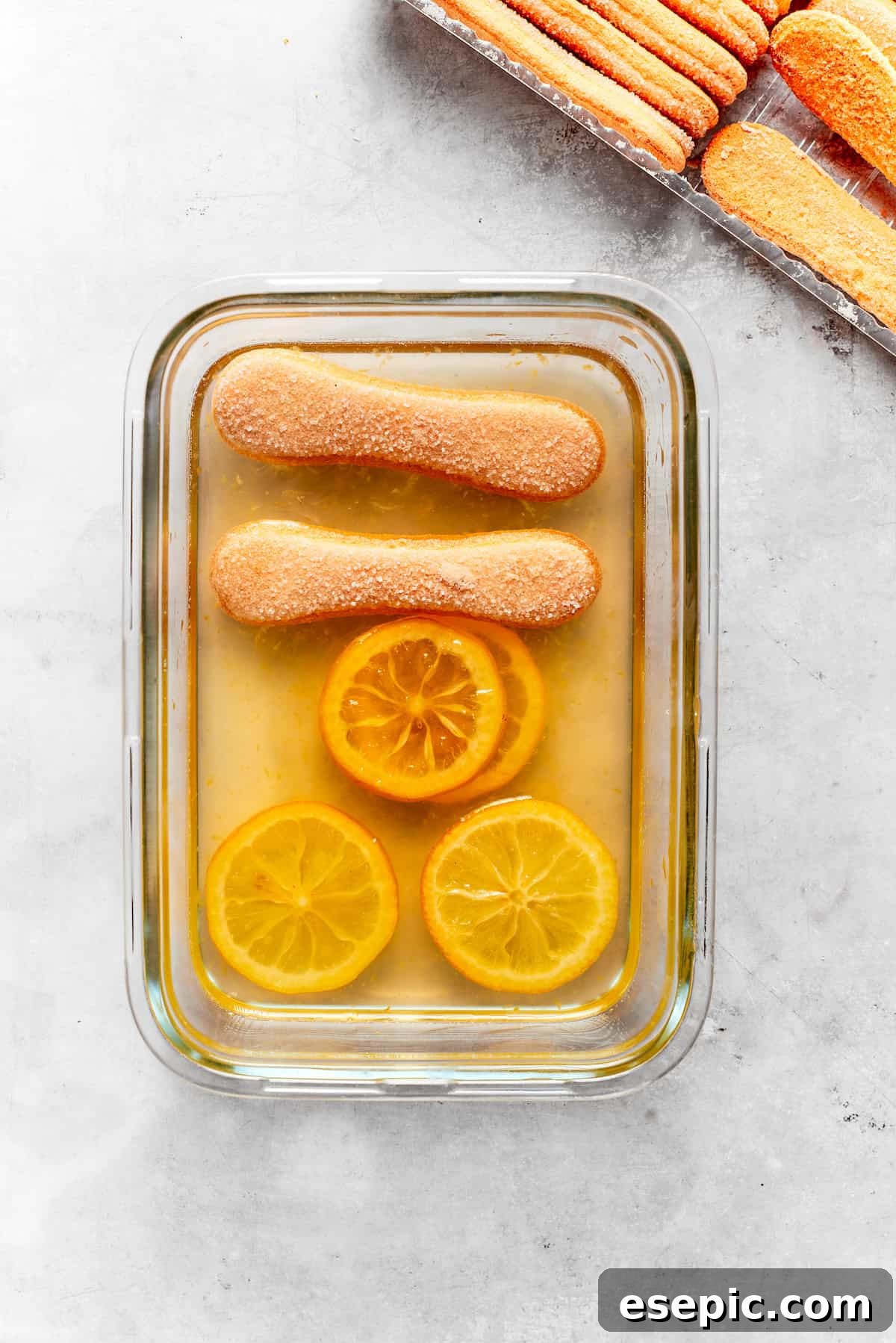 Lemon syrup and ladyfingers being carefully placed in a baking dish, forming the first layer.