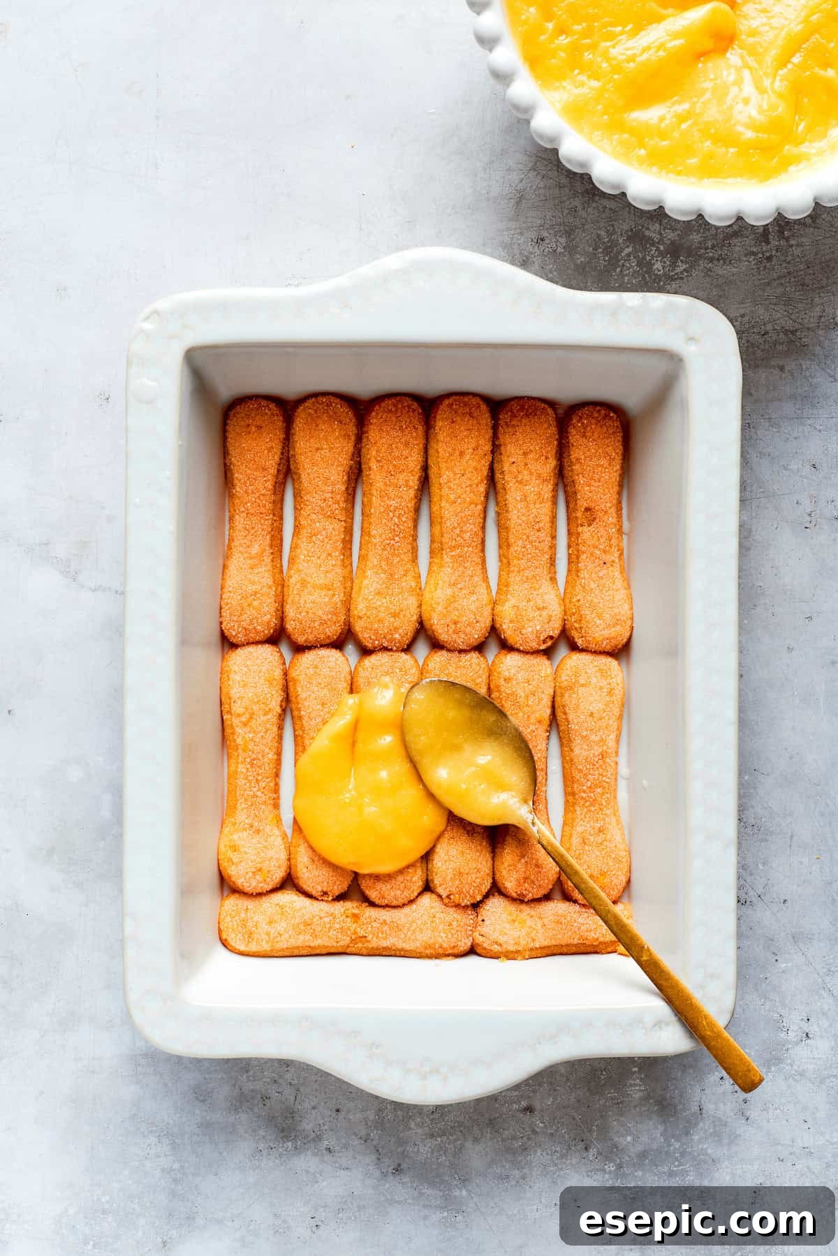 A generous layer of homemade lemon curd is spread evenly over the ladyfinger cookies.