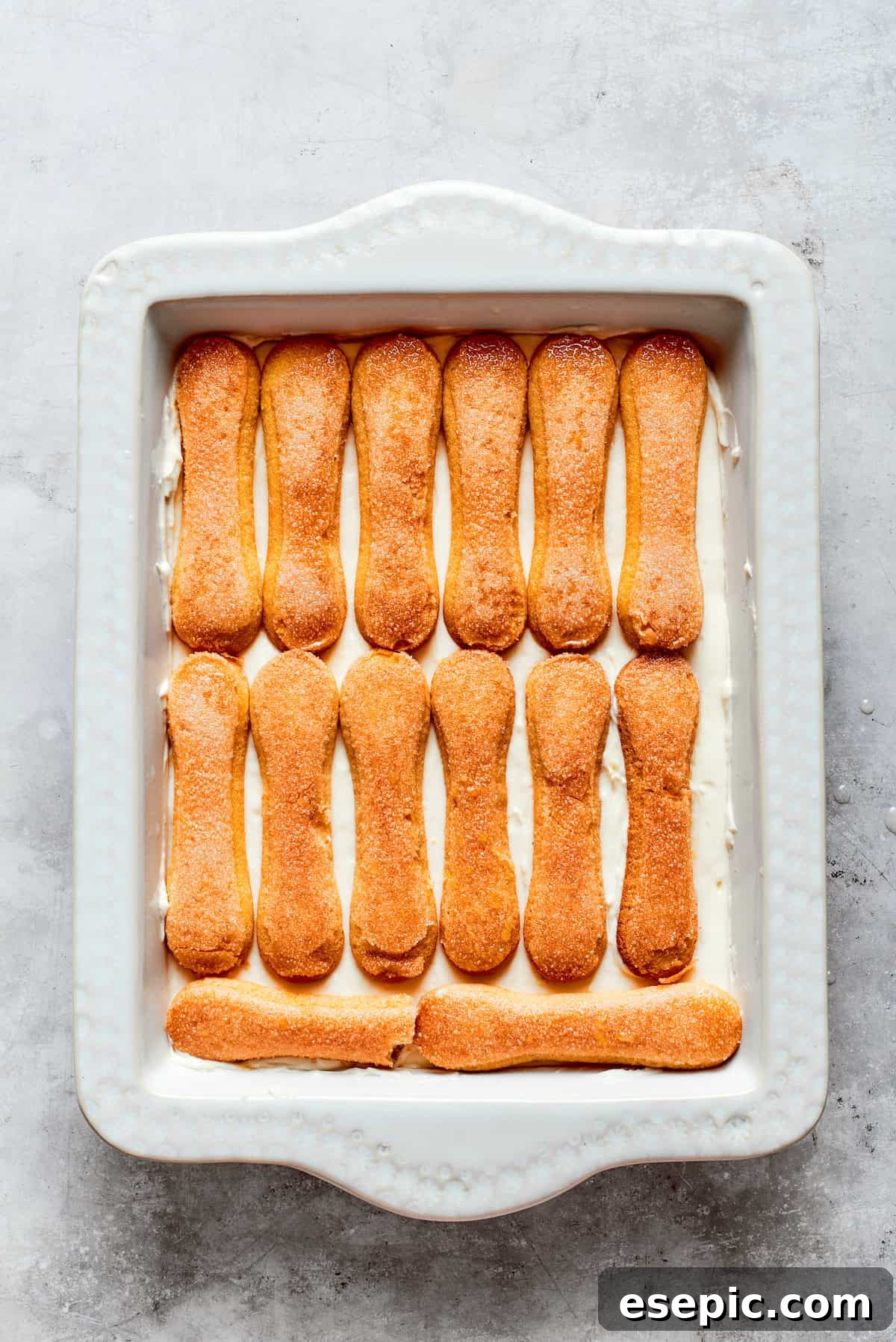 More ladyfinger cookies are meticulously placed on top of the mascarpone cream, preparing for the next layer.