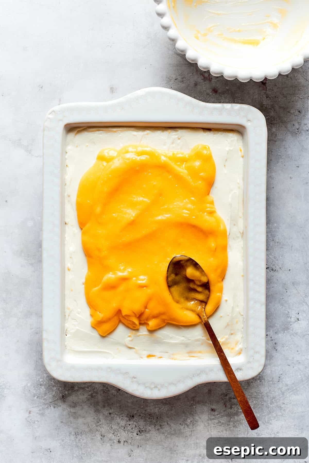 The final layer of smooth, bright lemon curd is spread over the top of the assembled tiramisu.