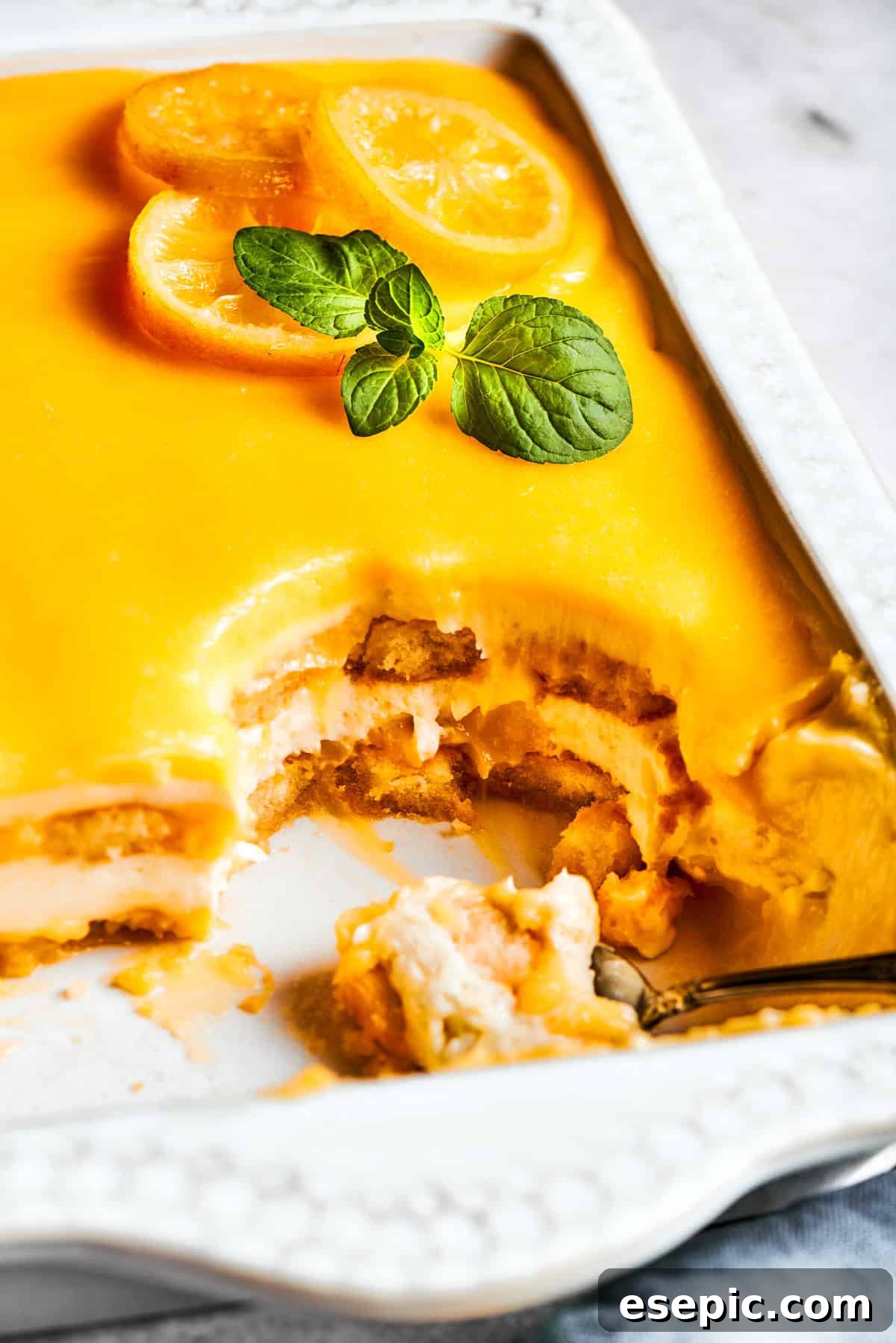 Half of a pan of lemon tiramisu with several square pieces already cut out and served, revealing the distinct layers.