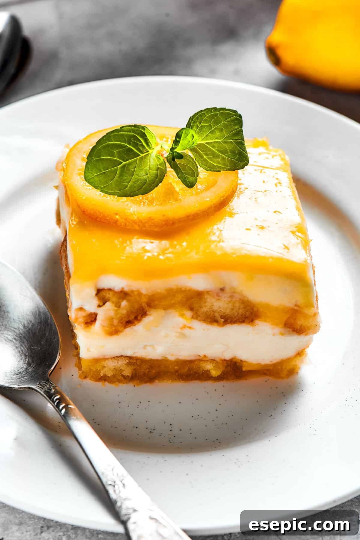 A square of lemon tiramisu on a white plate, elegantly garnished with fresh basil leaves for a pop of color and herbaceous note.