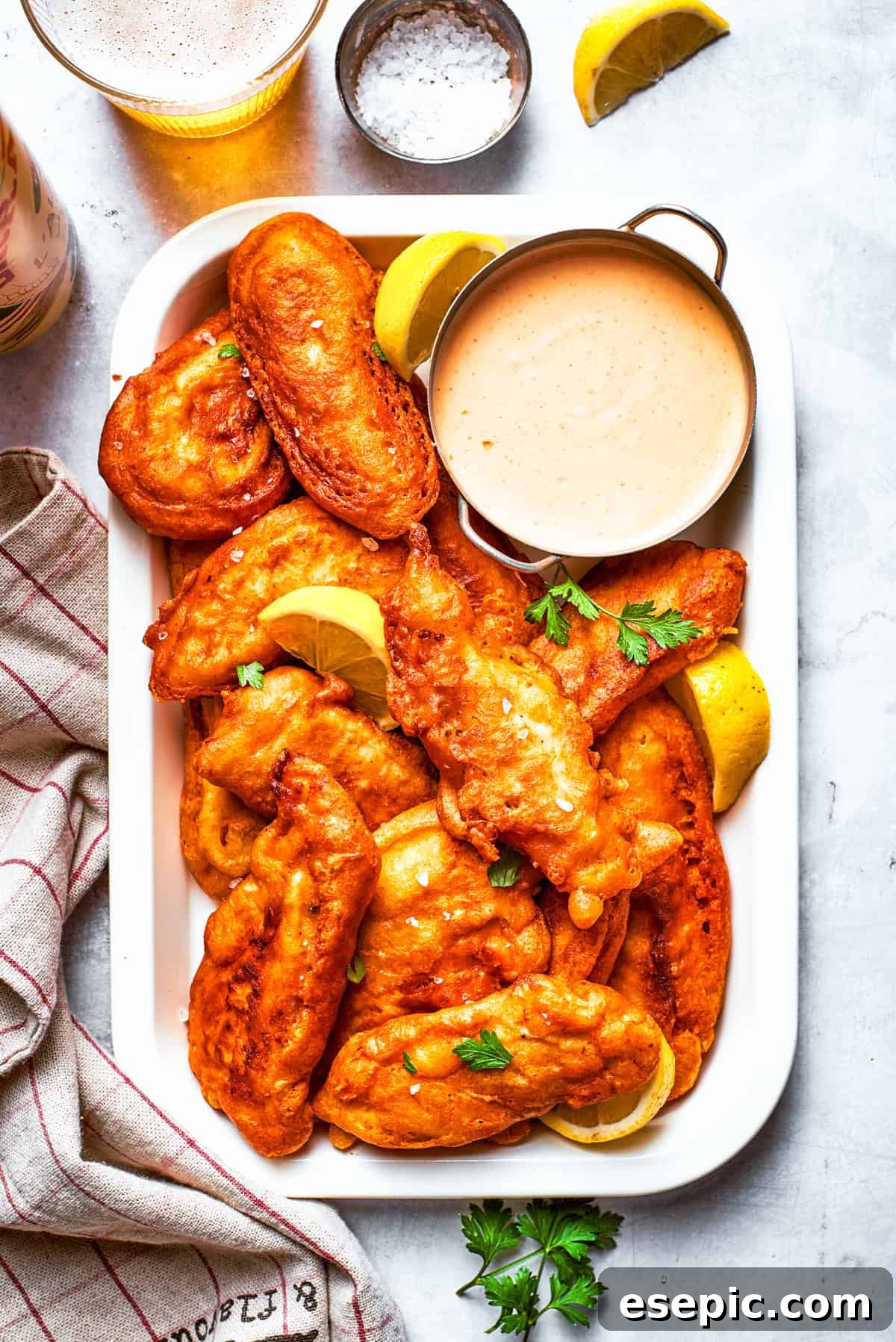 Pieces of beer battered chicken arranged on a rectangular serving plate with a bowl of dipping sauce.