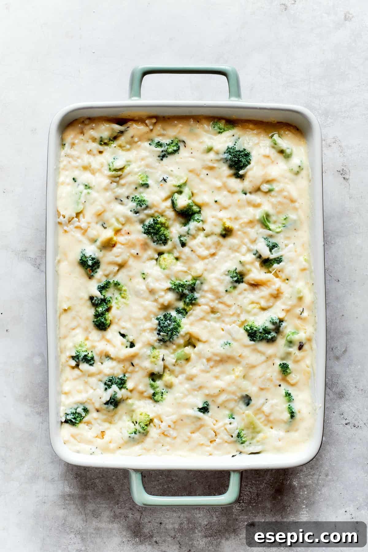Cooked broccoli and rice are gently mixed into the creamy cheese sauce within a baking pan, preparing for the casserole assembly.