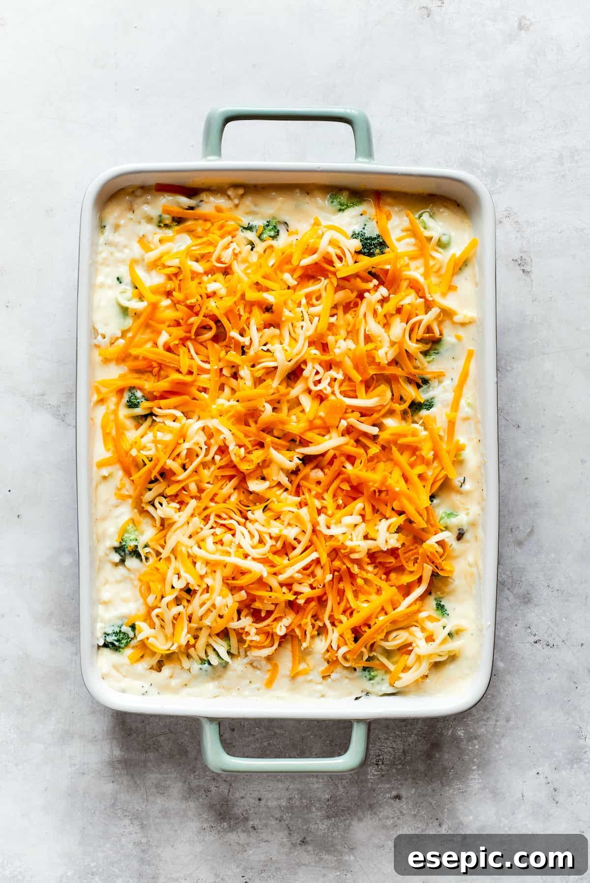 A generous layer of shredded cheese is sprinkled over the top of the broccoli & rice casserole before baking.